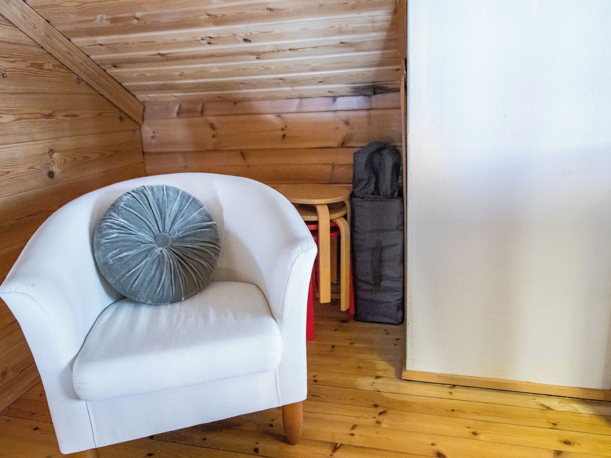 A white armchair with a grey pillow in a wooden cabin room.