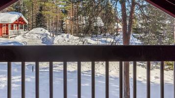 A cabin with a red exterior and a porch, surrounded by snow-covered ground and trees.