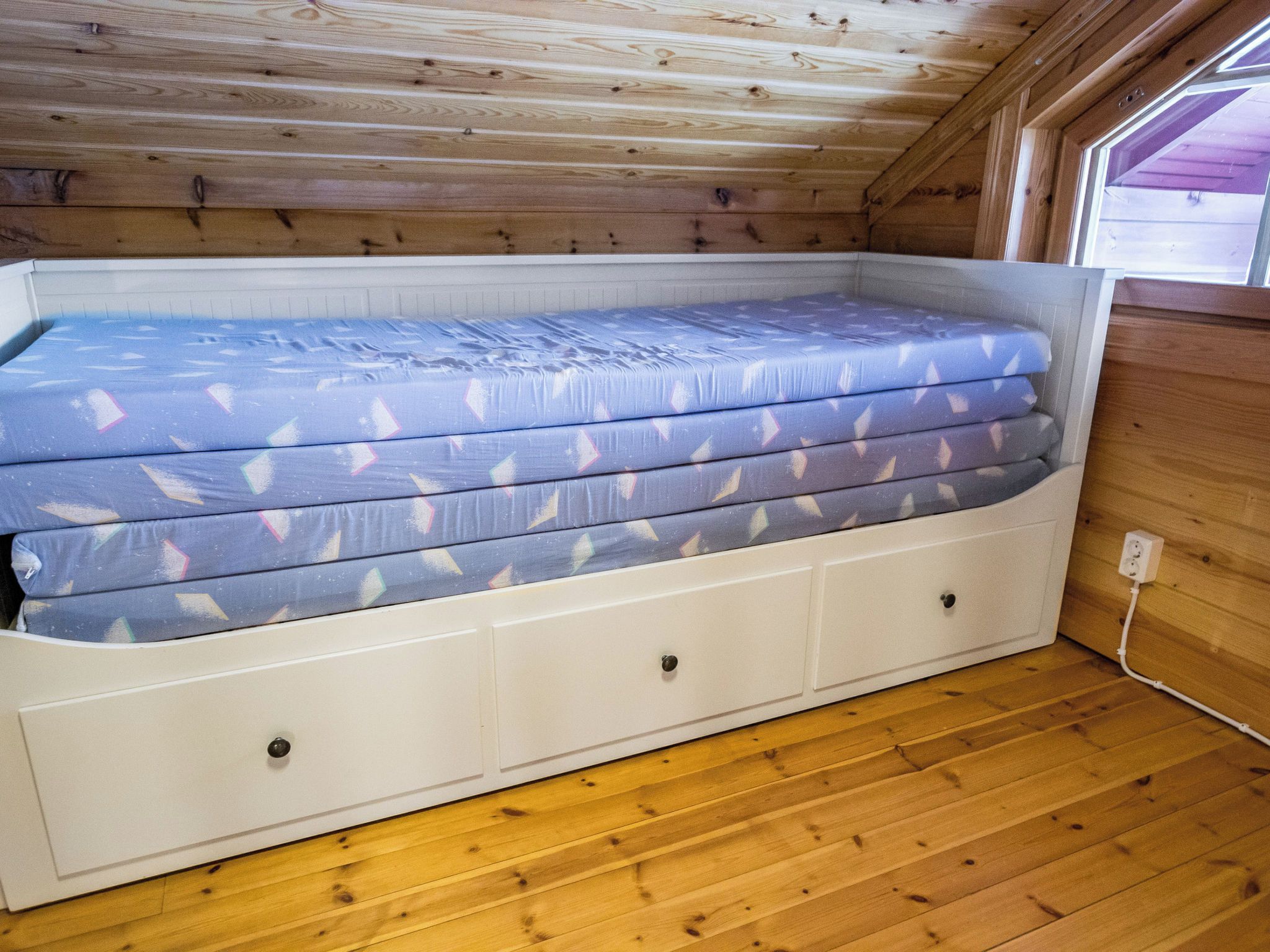 Un lit superposé avec un matelas orné d’un motif géométrique, une tête de lit blanche et un plancher en bois.