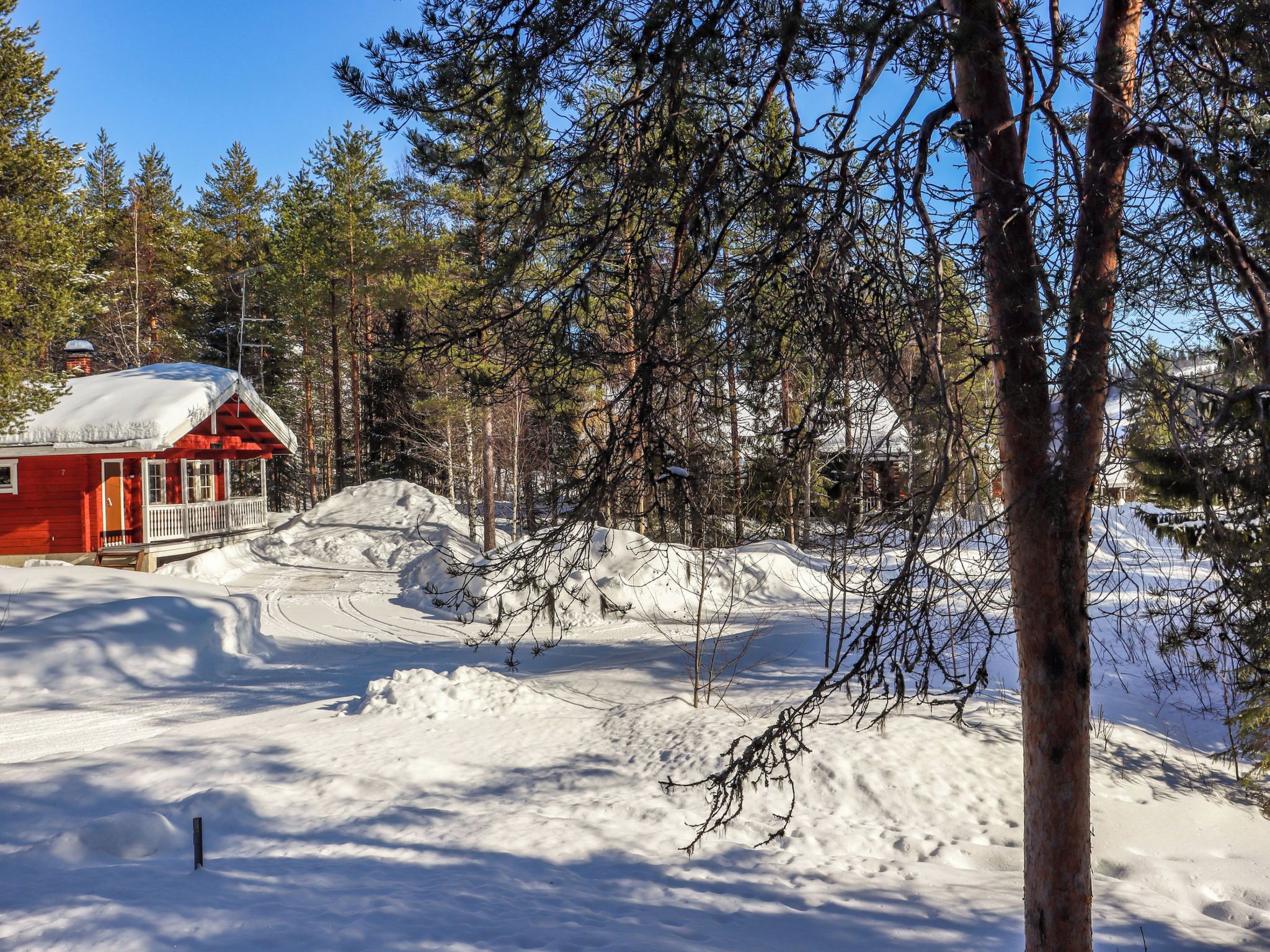 Eine rote Holzhütte mit schneebedecktem Dach, umgeben von Wald und Schnee.