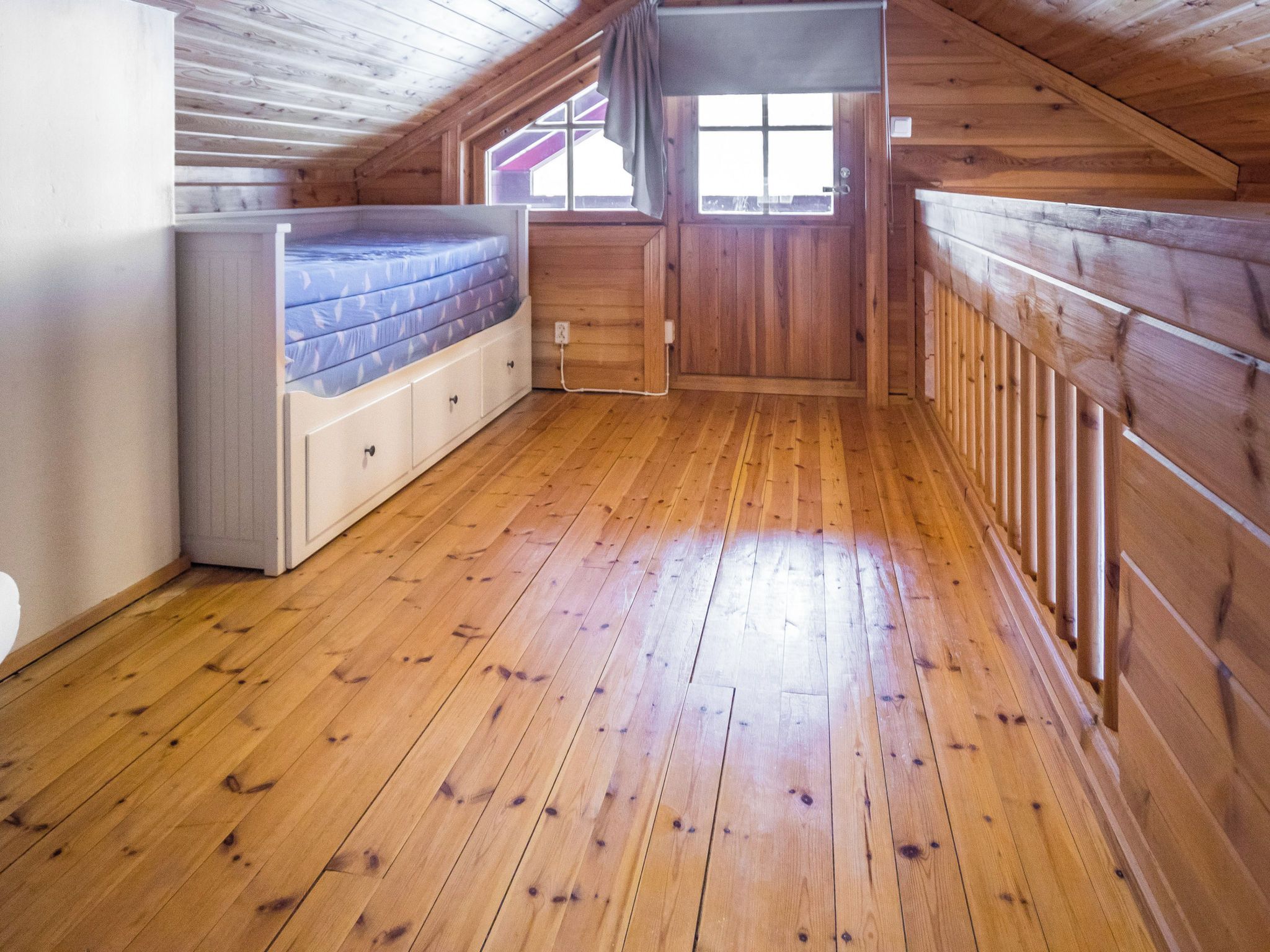A room with wooden walls and floor, a bunk bed, a window, and a door.