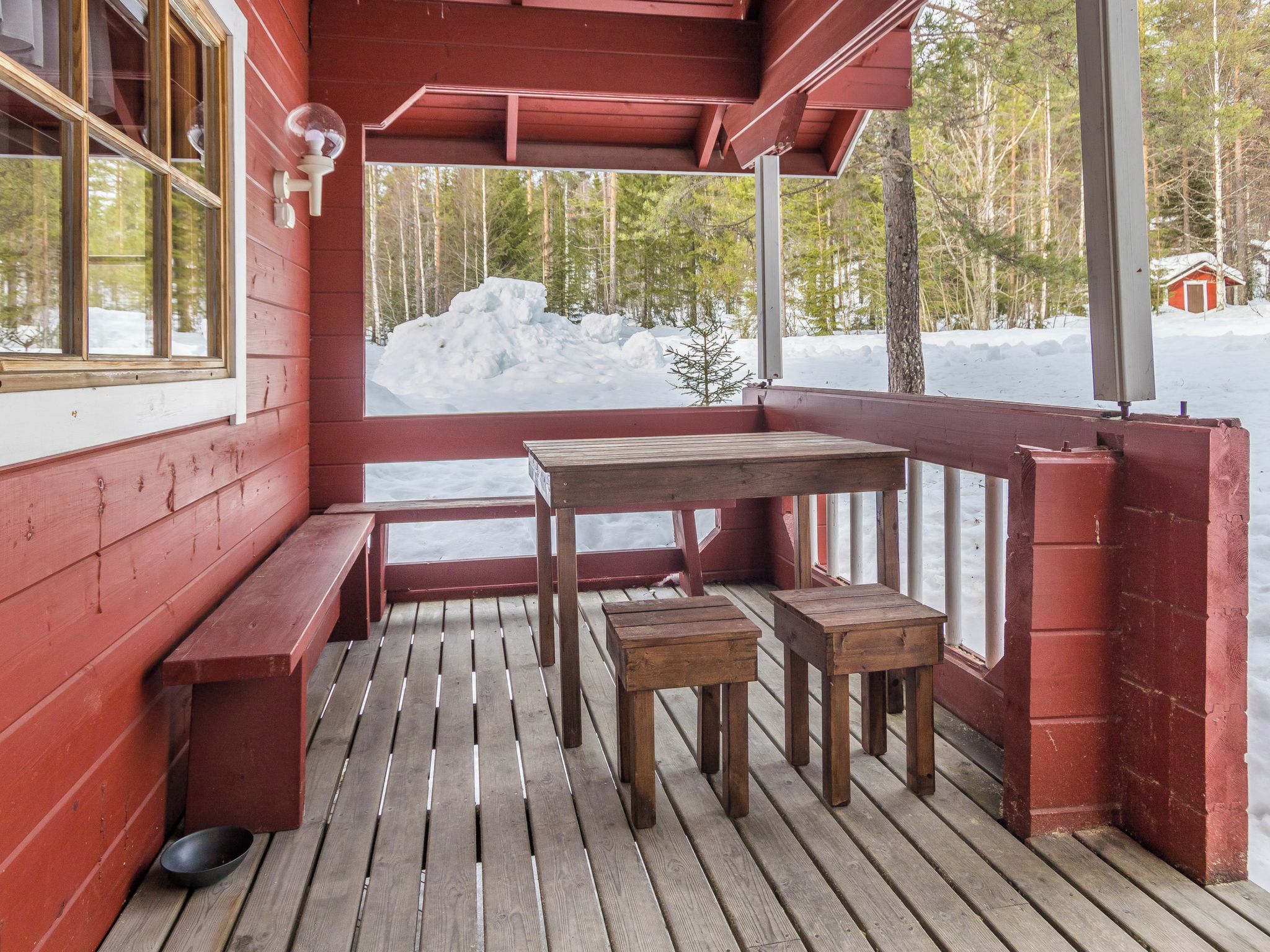 Una terraza de madera con bancos y una mesa, con vistas a un paisaje nevado y árboles.