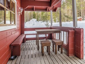 Una terraza de madera con bancos y una mesa, con vistas a un paisaje nevado y árboles.