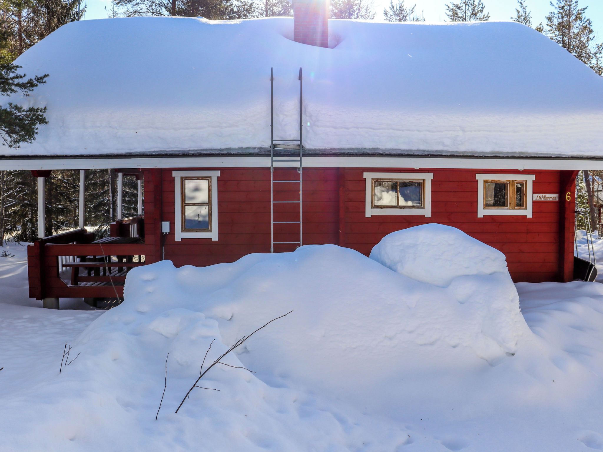 Eine rote Holzhütte mit verschneitem Dach, einer Leiter und einer kleinen Veranda.