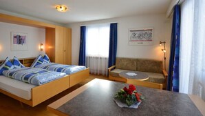 A modern hotel room with a bed, sofa, and a small table with a flower arrangement. - Haus Orion by Interhome (Saas-Fee)