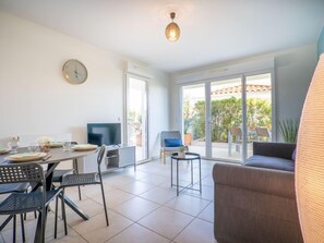 Un salon moderne comprenant un canapé, une table à manger pour quatre personnes, un téléviseur et une grande porte-fenêtre coulissante donnant sur une terrasse extérieure.