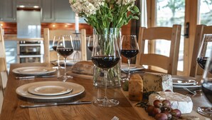 A wooden dining table set with plates, glasses, and a vase of flowers. - Croft Kincardine -  a lodge that sleeps 8 guests  in 4 bedrooms (Boat of Garten)