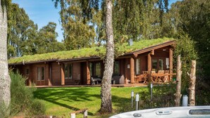 A wooden cabin with a grassy roof, surrounded by trees and a hot tub. - Croft Kincardine -  a lodge that sleeps 8 guests  in 4 bedrooms (Boat of Garten)