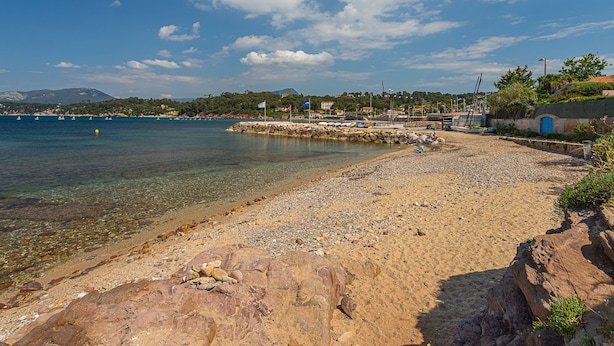 Une plage de galets bordée d’une eau claire, un rivage rocheux et, au loin, une chaîne de montagnes.
