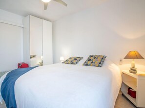 A bedroom with a large bed, a wardrobe, a bedside table with a lamp, and a suitcase on the floor. - Les Roches Bleues by Interhome (Le Pradet)