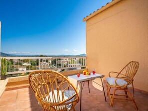 A balcony with wicker chairs and a table, overlooking a residential area with houses and mountains in the distance. - Les Roches Bleues by Interhome (Le Pradet)