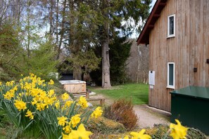 A wooden building with a hot tub and a garden with yellow flowers.