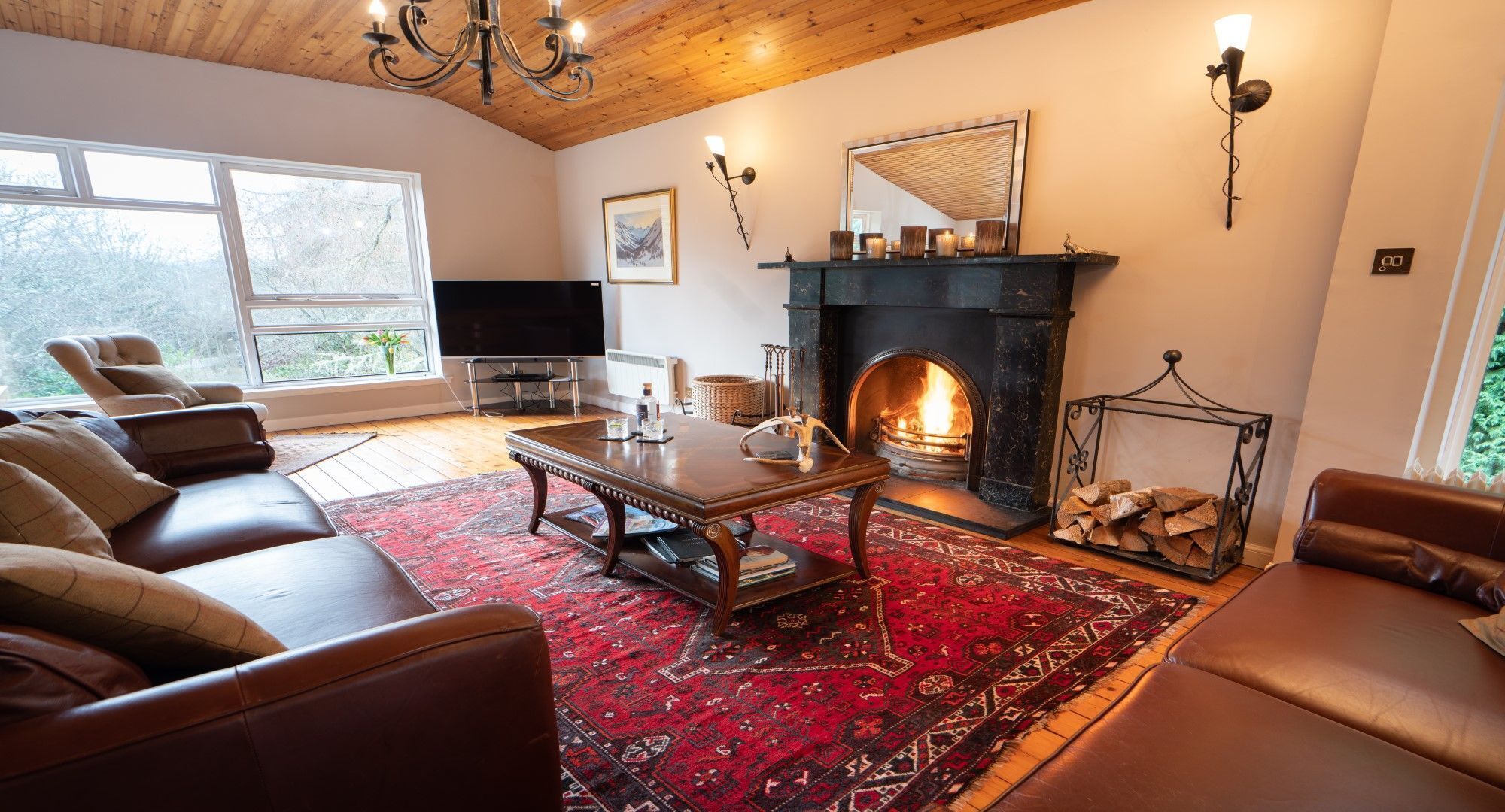 A cozy living room with leather sofas, a wooden coffee table, a fireplace, and a large window.