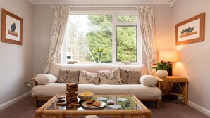 A cozy living room with a sofa, a coffee table with snacks and playing cards, a lamp, and framed pictures on the walls. - Four Pines Lodge -  a house that sleeps 8 guests  in 4 bedrooms (Dulnain Bridge)