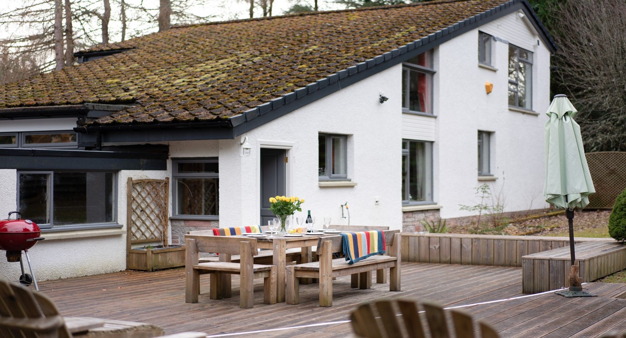 A house with a tiled roof, a deck with wooden furniture, and a barbecue grill.