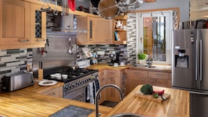 A modern kitchen with wooden cabinets, stainless steel appliances, and a hanging pot rack. - River House Garden Rooms -  a house that sleeps 2 guests  in 1 bedroom (Aviemore)
