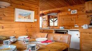 Interior de una cabaña de madera con comedor, cocina y un cuadro con un paisaje.