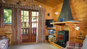 Un acogedor interior de cabaña con sofás de cuadros, un estufa de leña, un televisor y una ventana con cortinas.