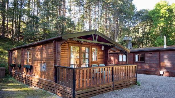 Una cabaña de madera con porche, rodeada de árboles.