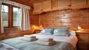 Un dormitorio de cabaña de madera con una cama, dos lámparas de noche y una ventana con cortinas.