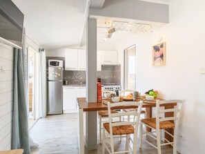 A modern kitchen with white cabinets, a stainless steel refrigerator, a microwave, and a gas stove. There is a dining table with four chairs and a chandelier above. - Apartment Bleuet by Interhome (Mimizan)