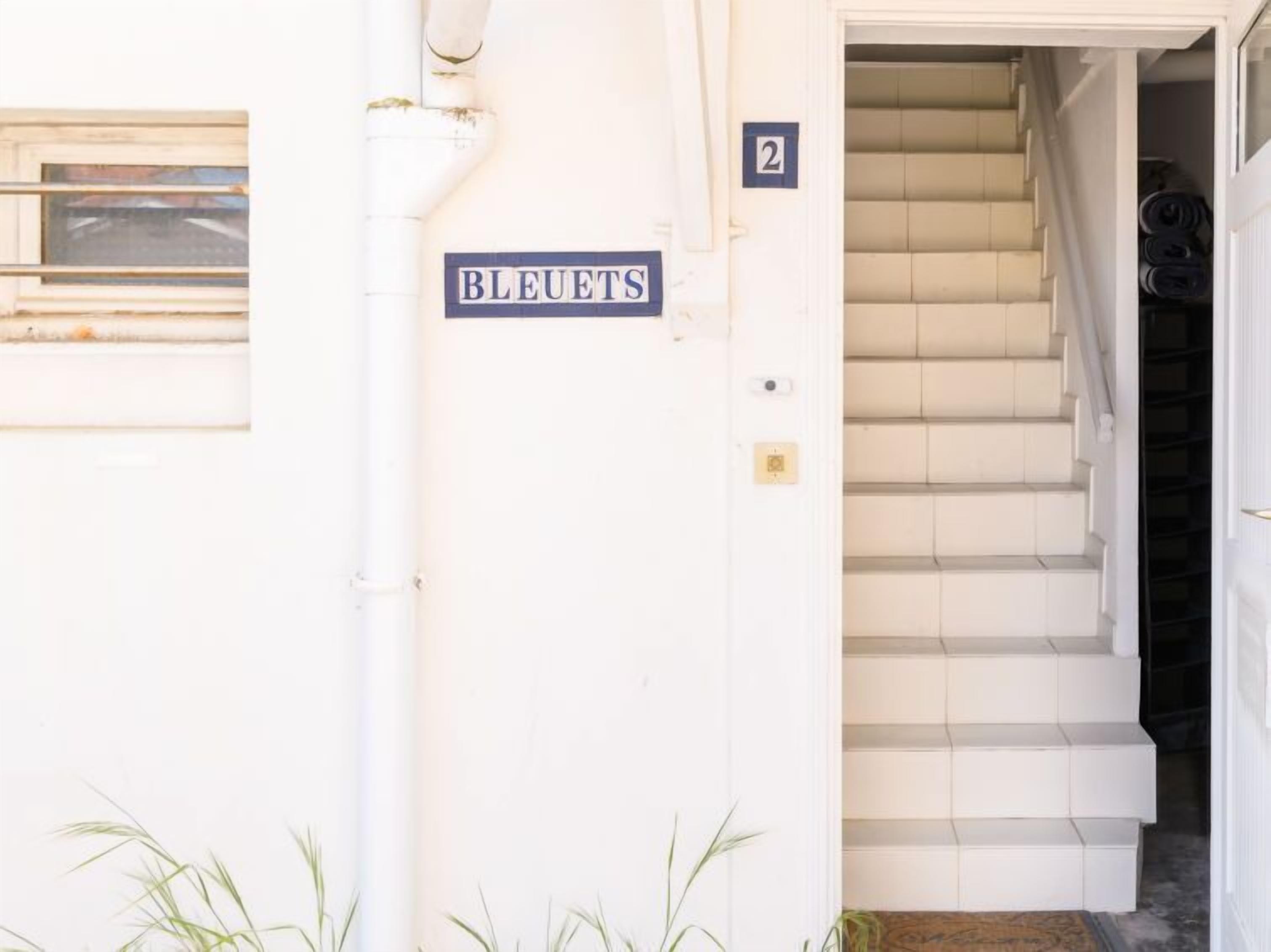 Entrada de un edificio con un letrero que dice “BLEUETS” y una escalera que conduce al interior.