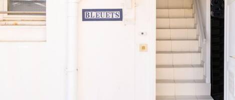 Entrada de un edificio con un letrero que dice “BLEUETS” y una escalera que conduce al interior.