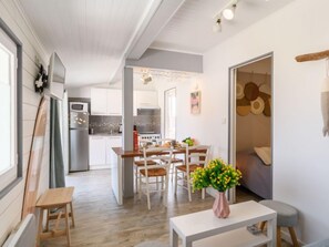 A modern kitchen with white cabinets, a dining area with a wooden table and chairs, and a small seating area with a white table and a vase of flowers. - Apartment Bleuet by Interhome (Mimizan)