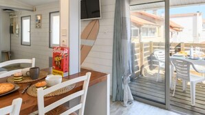 Comedor con mesa de madera, sillas blancas, televisor montado en la pared y vista al patio exterior.