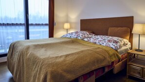 A hotel room with a bed, a nightstand, a window with curtains, and a view of a snowy landscape. - Harrachov 561 by Interhome (Harrachov)