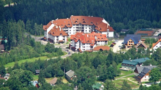 A large, multi-story building with a red-tiled roof, surrounded by dense forest. - Harrachov 561 by Interhome (Harrachov)
