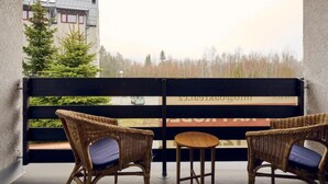 A balcony with wicker chairs and a small table, overlooking a road and trees. - Harrachov 561 by Interhome (Harrachov)