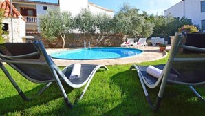 Une piscine avec des chaises longues, un mur en pierre et un bâtiment doté d’un toit en tuiles.