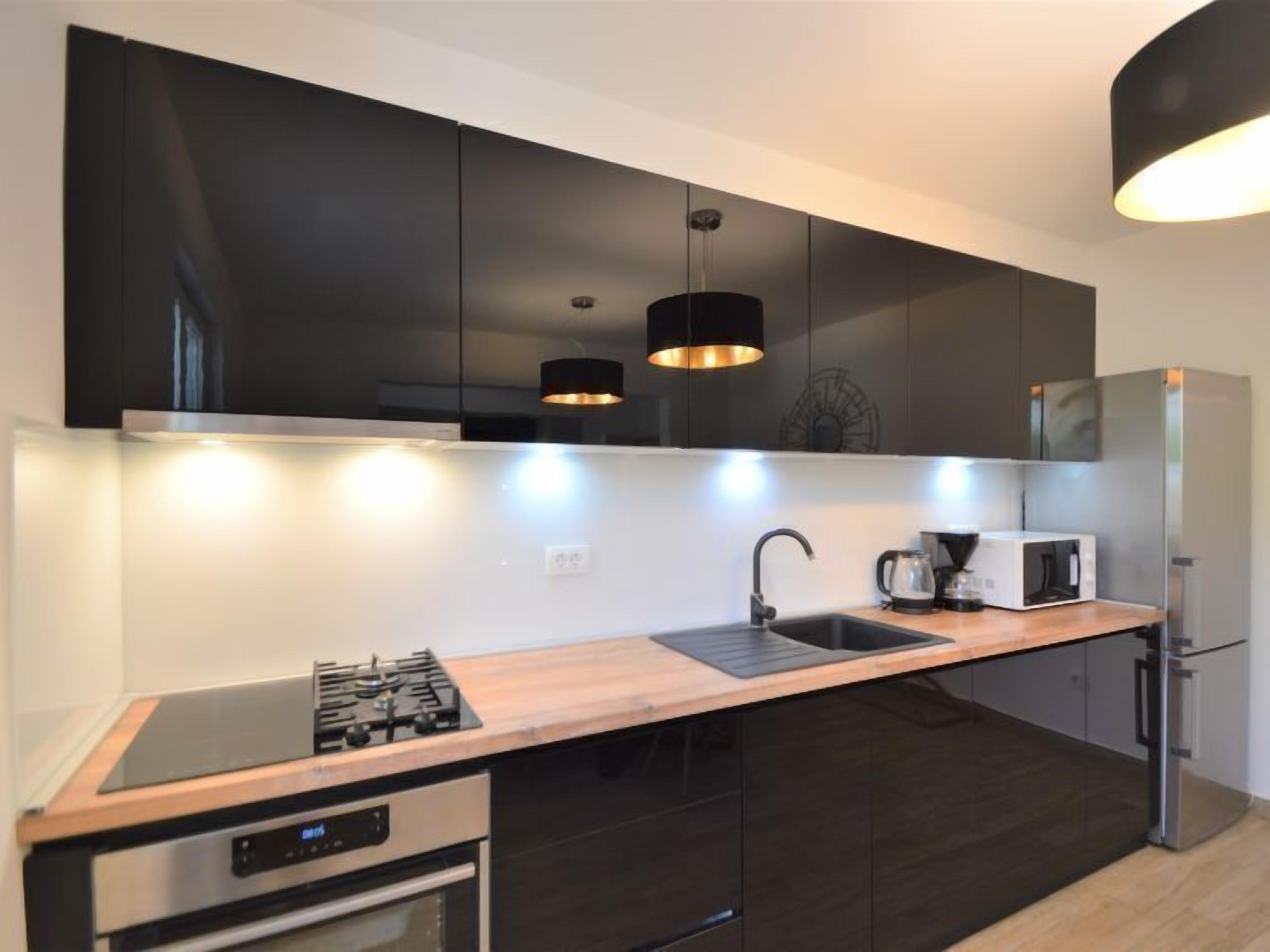 Una cocina moderna con armarios oscuros, un refrigerador de acero inoxidable, un microondas, una estufa a gas e iluminación colgante.