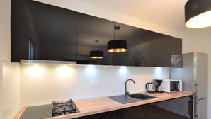 Une cuisine moderne avec des meubles de couleur sombre, un réfrigérateur en acier inoxydable, un four à micro-ondes, une cuisinière à gaz et des luminaires suspendus.