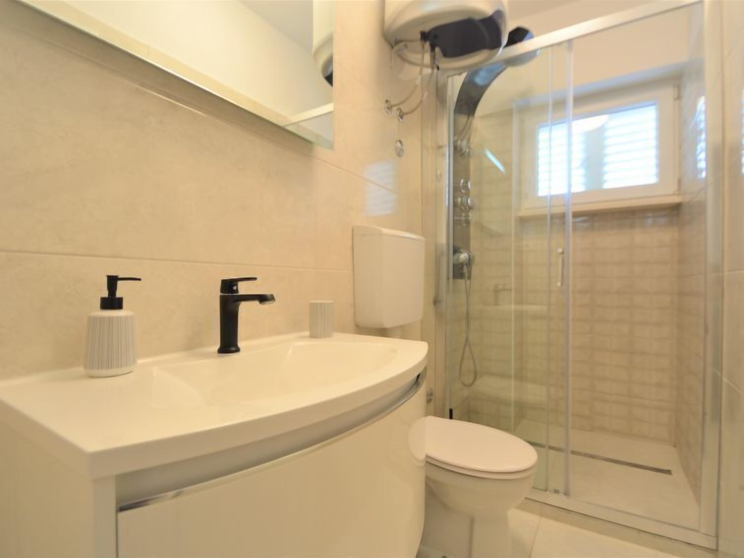 A modern bathroom with a curved white sink, black faucet, and a toilet.