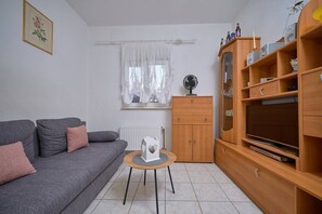Un salon avec un canapé gris, une petite table en bois, un meuble avec des étagères et un radiateur.