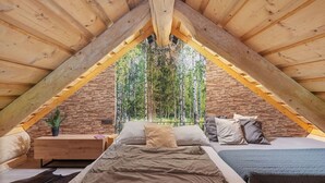 A cozy attic bedroom with a sloped wooden ceiling, a stone wall, and a large window offering a view of trees. - Vacation home KuŘíp by Interhome (Benesov nad Cernou)