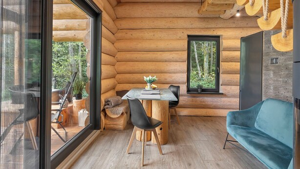 A log cabin interior with a dining area, a sofa, and a large window offering a view of trees. - Vacation home KuŘíp by Interhome (Benesov nad Cernou)