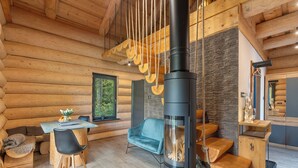A log cabin interior with a central wood-burning stove, a dining area with a table and chairs, and a cozy seating area with a blue sofa. - Vacation home KuŘíp by Interhome (Benesov nad Cernou)