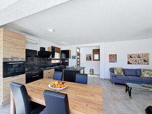 A modern kitchen with black appliances, a dining table with fruit, and a living area with a sofa and artwork.