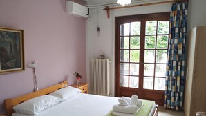 Una cama bien hecha con ropa blanca, una toalla verde y un cabecero de madera. Se ve una ventana con vistas a la vegetación, y un radiador en la pared.