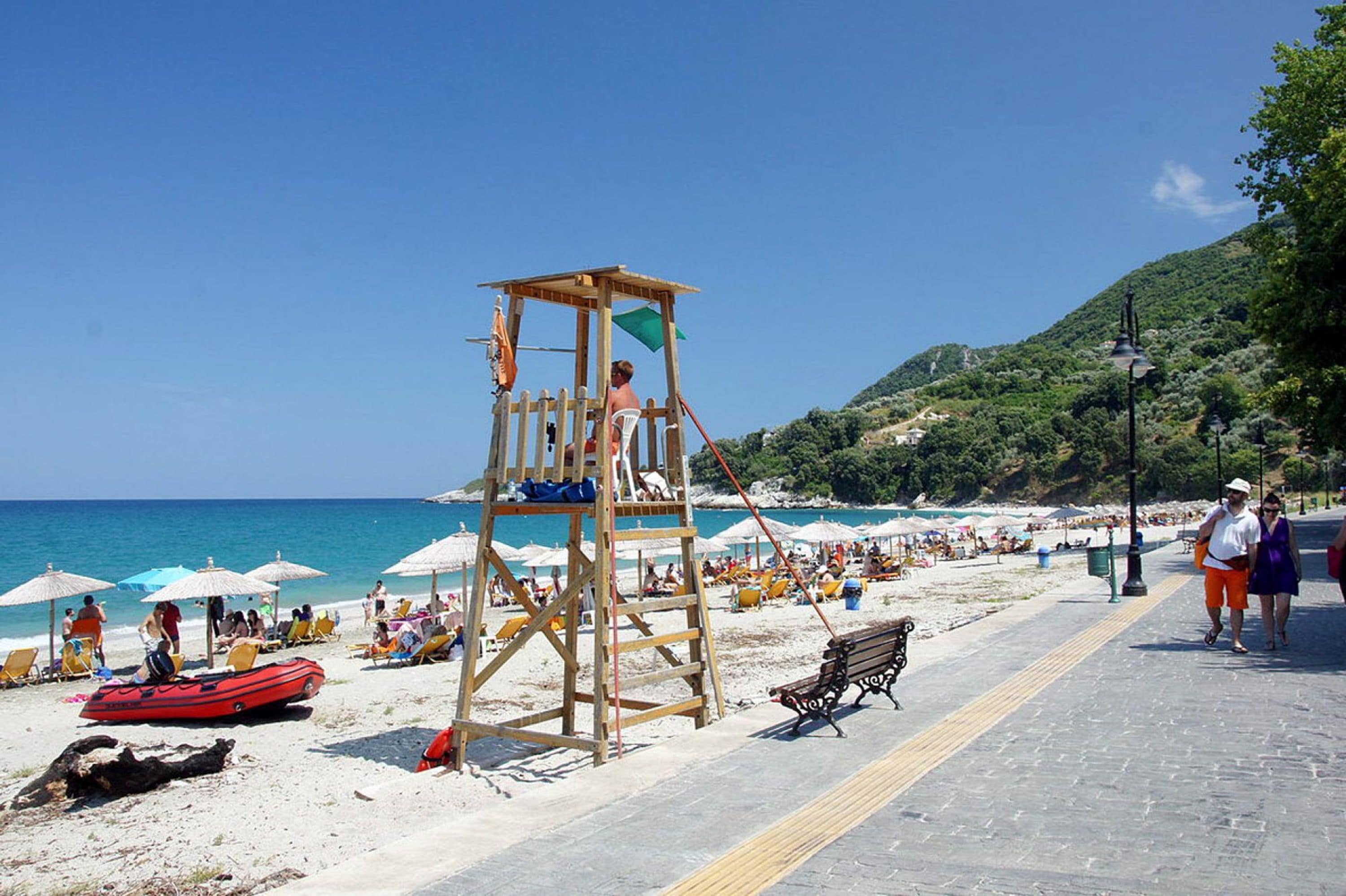 A beach with a lifeguard tower, beach umbrellas, and a paved walkway.