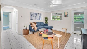 Een woonkamer met een blauwe bank, een kleurrijke stoel, een klein tafeltje en een plafondventilator.
