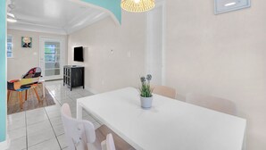 Een moderne woonkamer met een witte eettafel, een potplant en een kleurrijke stoel.