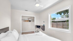 A bedroom with a bed, a desk, a chair, and a window with a view of a wooden fence and trees. - Charming 2BR Dania Beach Bungalow Getaway (Dania Beach)