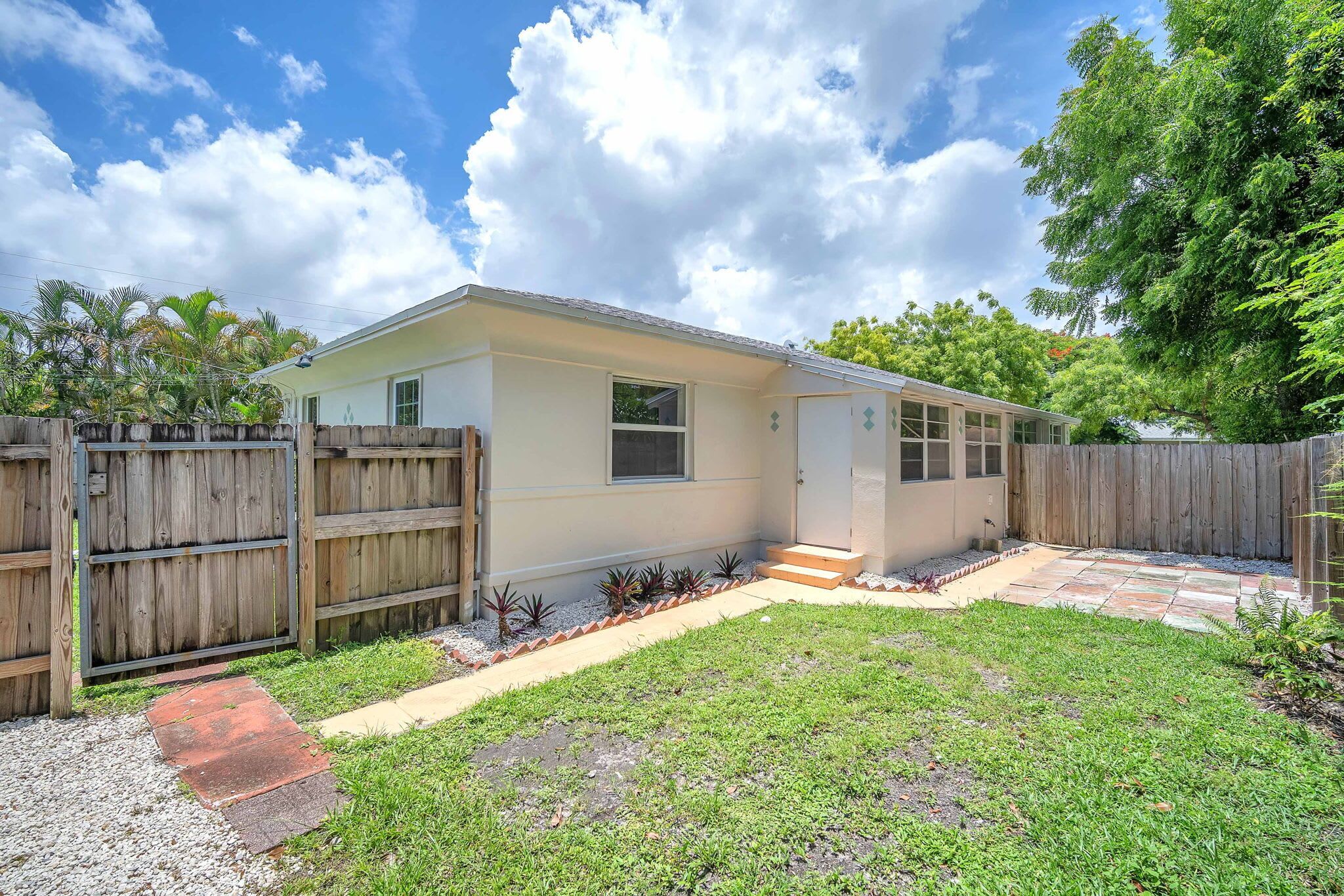 A single-story house with a front yard, a wooden fence, and a small garden area.