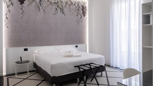 A modern hotel room with a large bed, a side table, a chair, and a view of the outdoors through sheer curtains. - Domea Superior Rooms (Reggio Calabria)