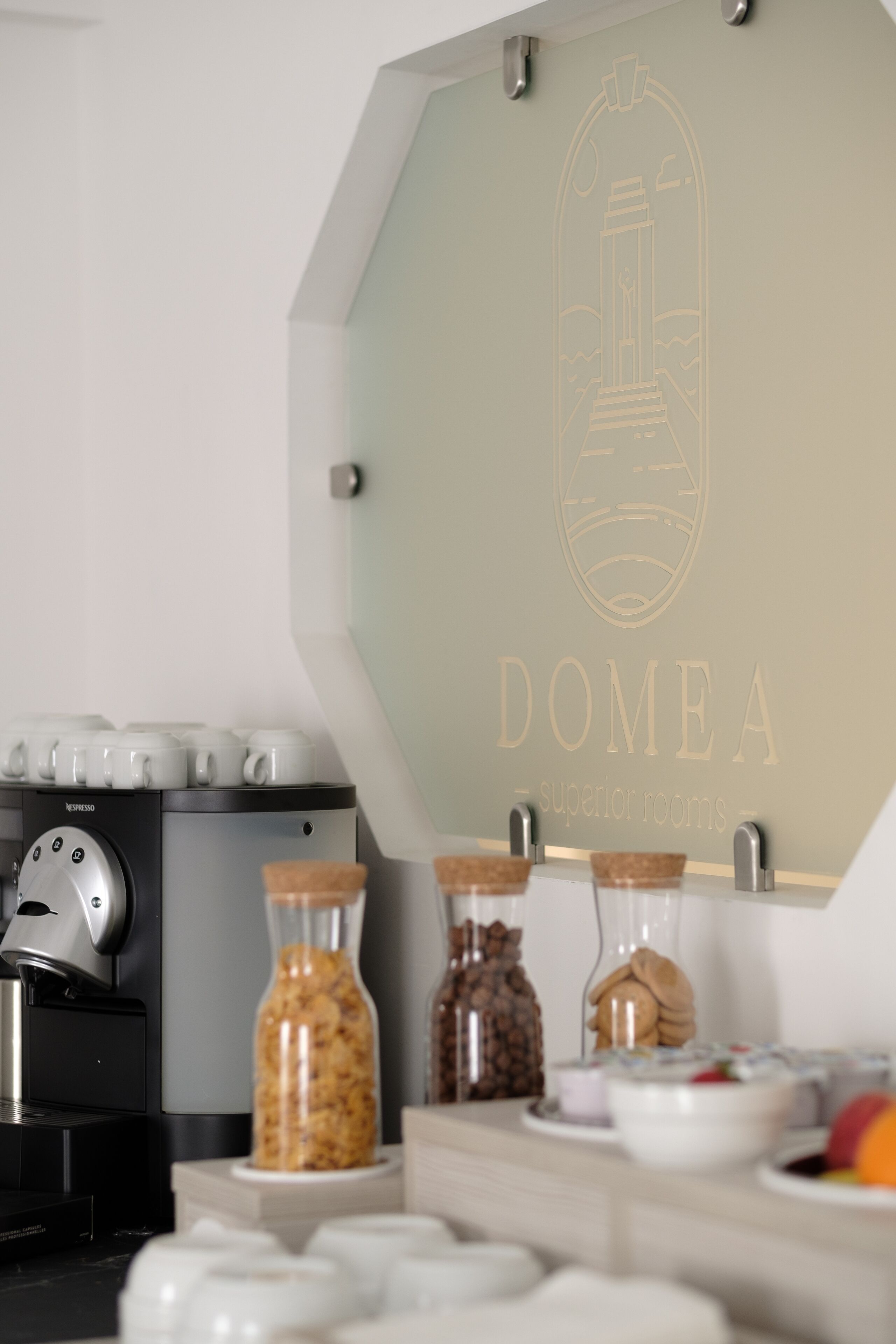 A coffee station with a Nespresso machine, jars of snacks, and a sign reading "DOMEA - superior rooms".