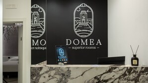 A hotel reception desk with a marble counter, a digital screen displaying the hotel name, and a logo above the reception area. - Domea Superior Rooms (Reggio Calabria)